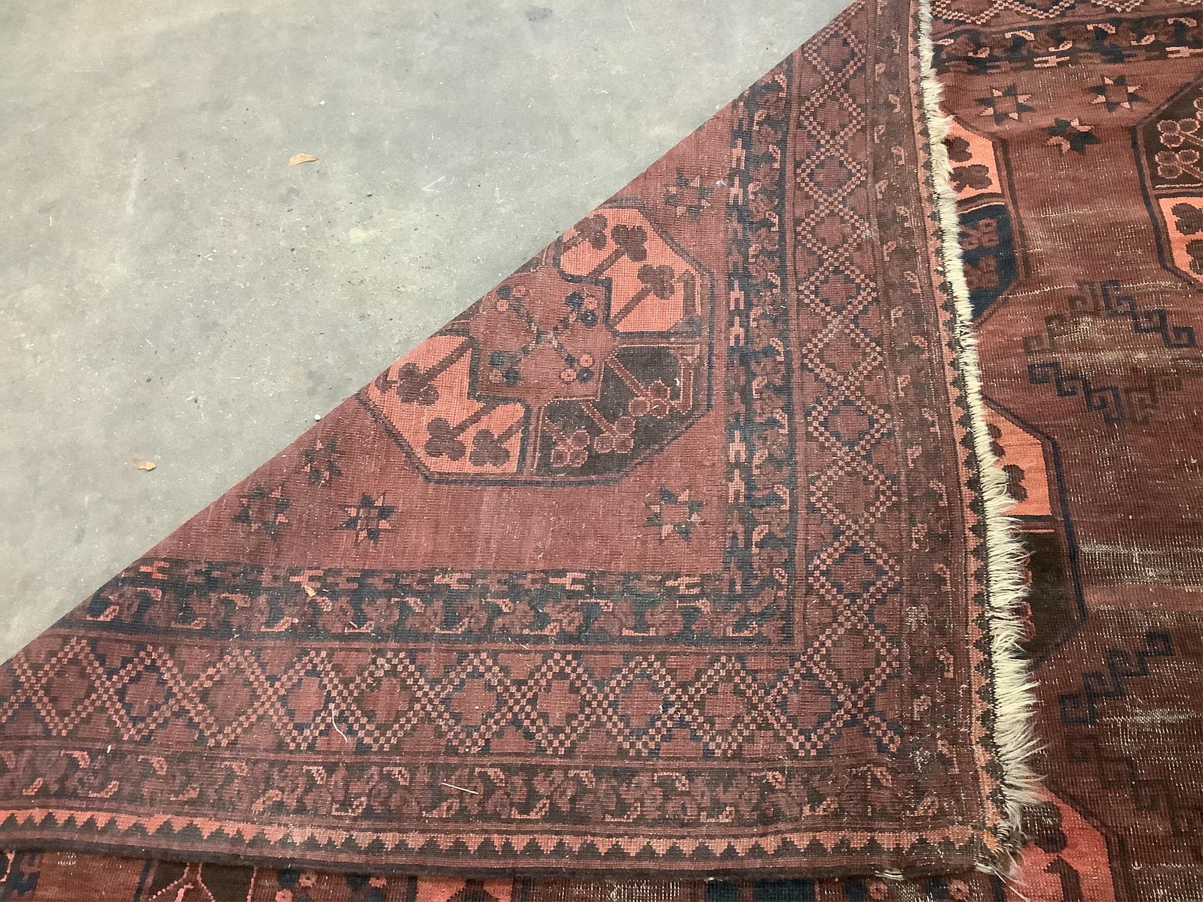 An Afghan red ground carpet, 380 x 240cm. Condition - poor to fair, one area of patching and several areas of low pile